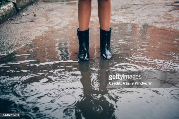 low section of teenager wearing rubber boot standing in puddle during rain - teen boots russian stock pictures, royalty-free photos & images