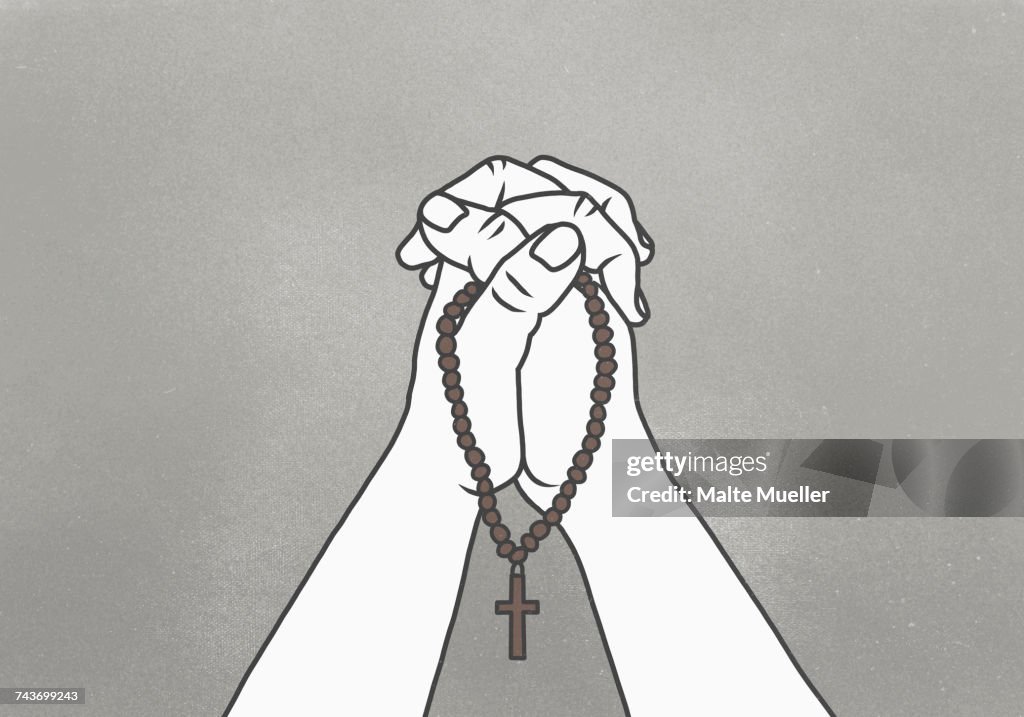 Cropped image of clasped hands holding rosary beads against gray background
