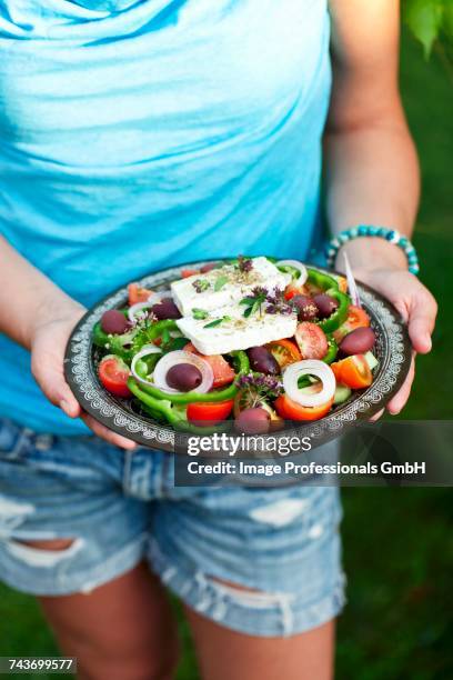 a woman holding a plate of greek salad - fetta stockfoto's en -beelden