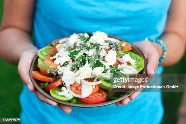 a woman holding a plate of greek salad - griechischer salat stock-fotos und bilder