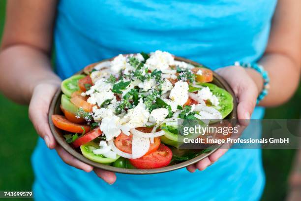 a woman holding a plate of greek salad - fetta stockfoto's en -beelden