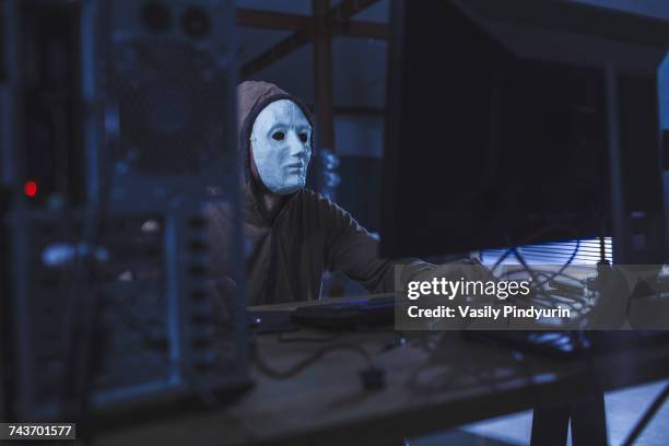 man wearing mask and hood using computer at table - anonymous mask stockfoto's en -beelden