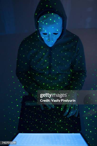 high angle view of green lights over computer hacker wearing mask using laptop - anonymous mask stockfoto's en -beelden