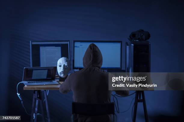 rear view of computer hacker sitting at desk with equipment against gray background - con man 個照片及圖片檔