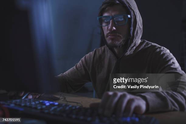 serious burglar wearing hooded shirt using computer at table - stalking photos et images de collection