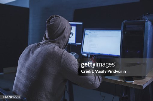 Computer hacker wearing hooded shirt using computer at table Computer hacker wearing hooded shirt using computer at table