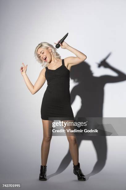 cheerful woman singing with microphone while standing against white background - pink - singer stock-fotos und bilder
