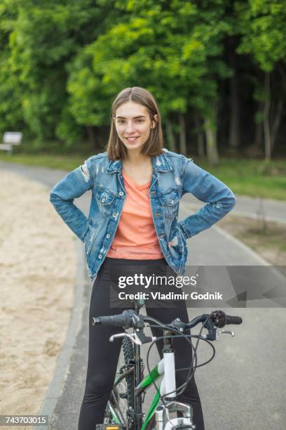 smiling portrait of woman with hands on hip sitting on bicycle at road in park - voronezh stock pictures, royalty-free photos & images