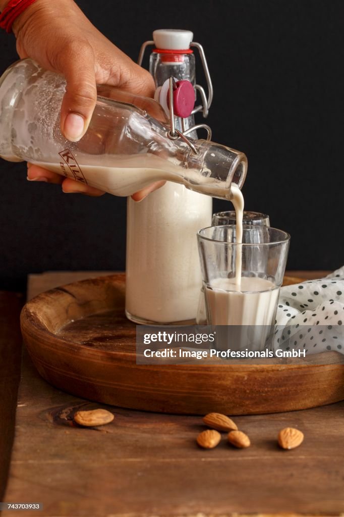 Homemade almond milk being poured from a flip-top bottle into a glass