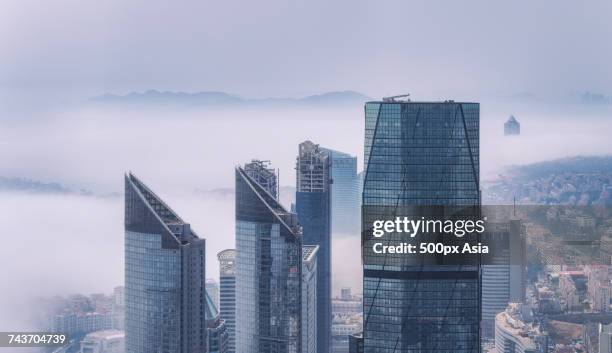 skyscrapers against buildings shrouded in fog, qingdao, shandong, china - many cities in china shrouded in fog photos et images de collection