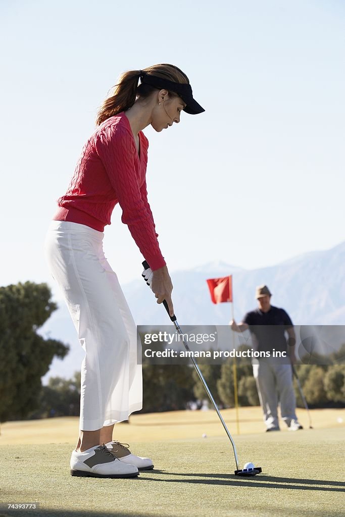 Woman playing golf, man holding golf flag