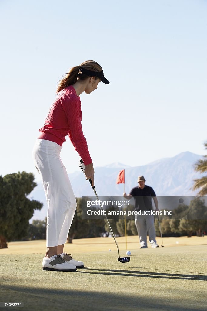 Woman playing golf, man holding golf flag