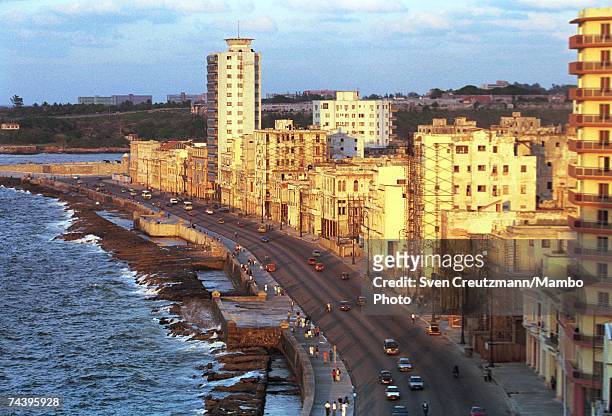 People stroll the sidewalks past vintage buildings at sunset on the coastal oceanfront Malecon highway on March 3, 2002 in Havana, Cuba.