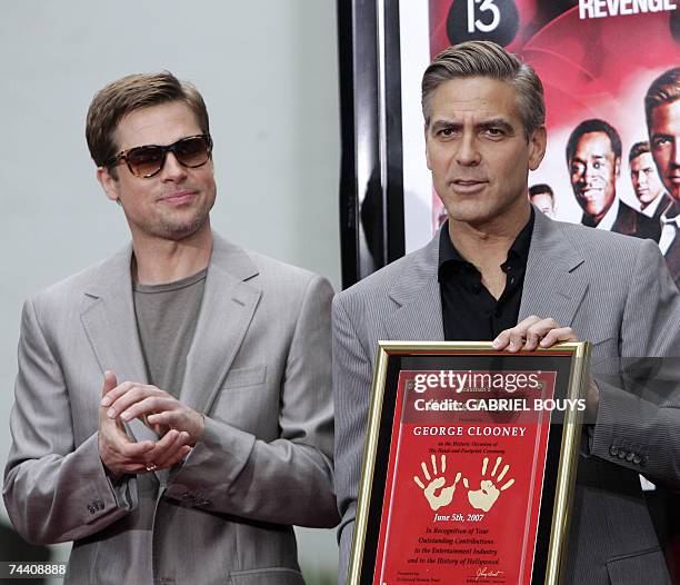 Hollywood, UNITED STATES: Brad Pitt as George Clooney poses with his plaque after both actors immortalized their prints in cement in the famed...