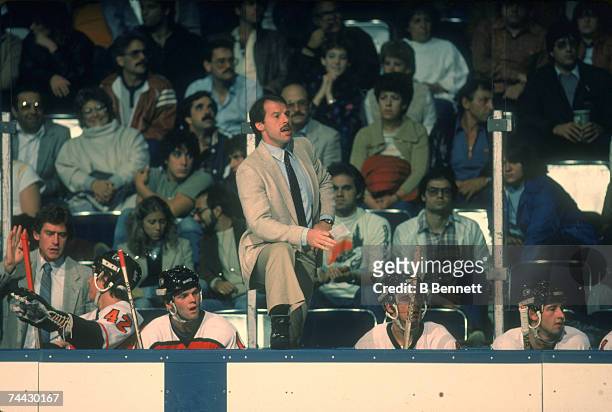 Canadian professional ice hockey coach Mike Keenan of the Philadelphia Flyers stand with one foot on the boards and watches the action from the bench...