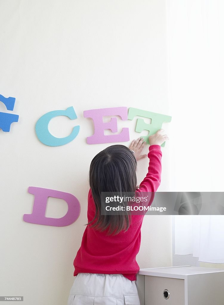 French girl putting alphabet on wall in room