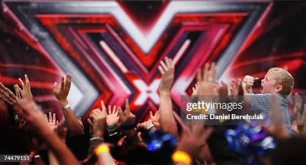 Young boy holds up his arms in an X as contestants welcome the judges during the first day of auditions for series 4 X Factor at Arsenal Emirates...