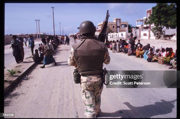 United Nations soldier walks down a road lined with Somali people June 6, 1993 in Mogadishu, Somalia. UN troops seized the residence of General...