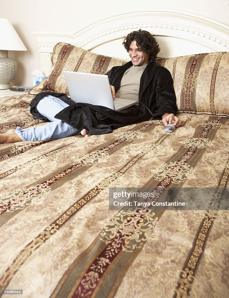 Hispanic man typing on laptop in bed