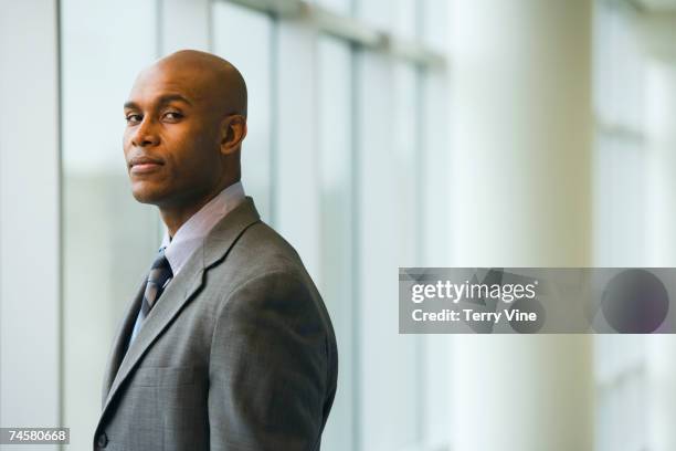 african businessman standing next to window - bald 30s stockfoto's en -beelden