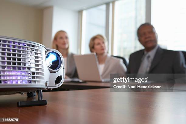slide projector on conference table, three businesspeople sitting in background - diaprojektor stock-fotos und bilder