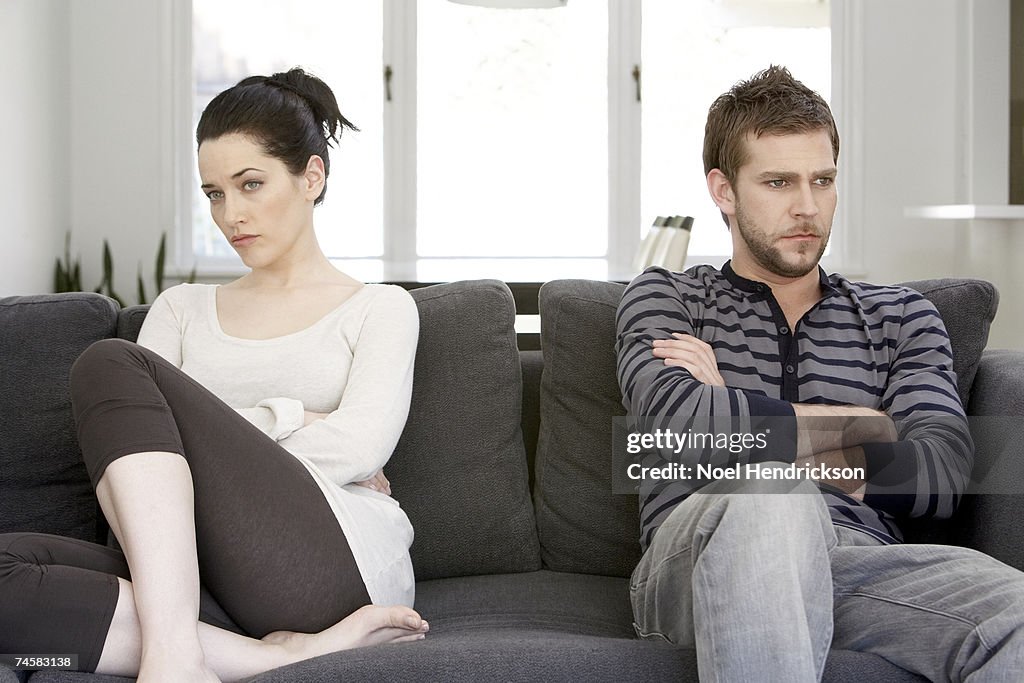 Couple sitting on sofa with arms folded, looking angry