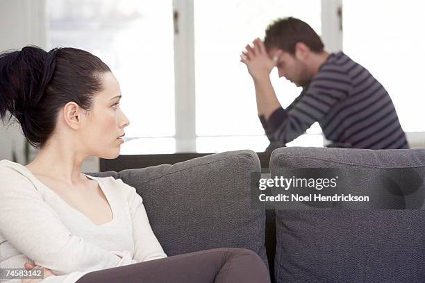 young woman sitting on sofa, looking at distressed man at table - dispute couple bildbanksfoton och bilder