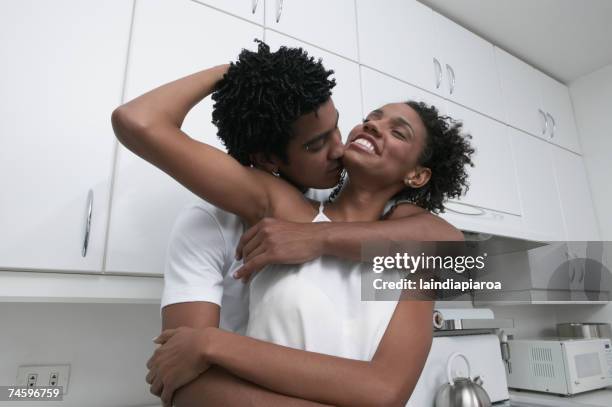 african couple hugging in kitchen - couple kiss kitchen stock pictures, royalty-free photos & images