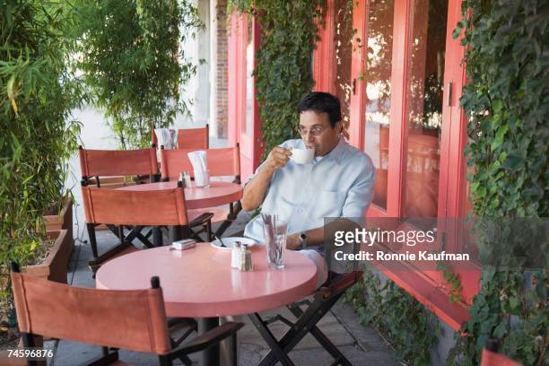 hispanic man drinking coffee at restaurant - té terraza fotografías e imágenes de stock