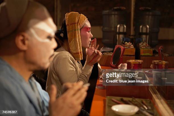 an old actor and young actress apply traditional chinese face paint backstage, preparing for a performance. - beijing opera stock pictures, royalty-free photos & images