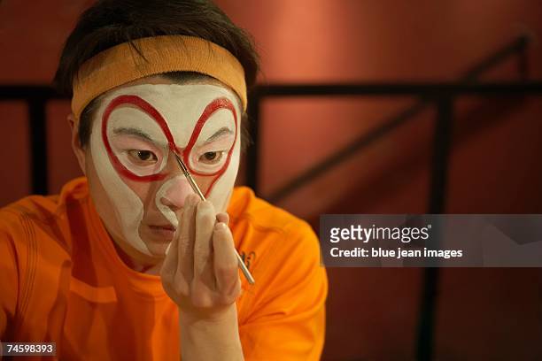 a young actor concentrates as he carefully brushes traditional chinese face paint around his eyes. - opera backstage stock pictures, royalty-free photos & images