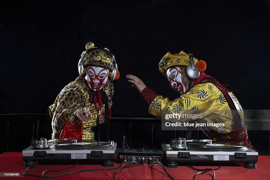 An actor dressed as a traditional Beijing Opera Monkey King and an actor dressed as a Comedian fool around and use a pair of DJ turntables.