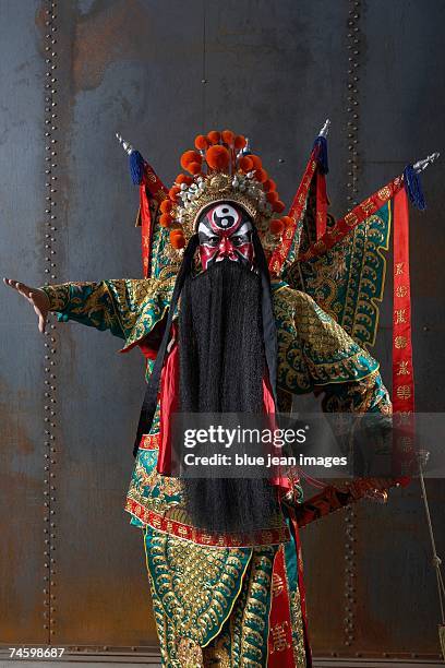 close up of an actor dressed as a traditional beijing opera army general posing in front of an industrial rusting steel wall with flags and a sword. - peking opera stock pictures, royalty-free photos & images