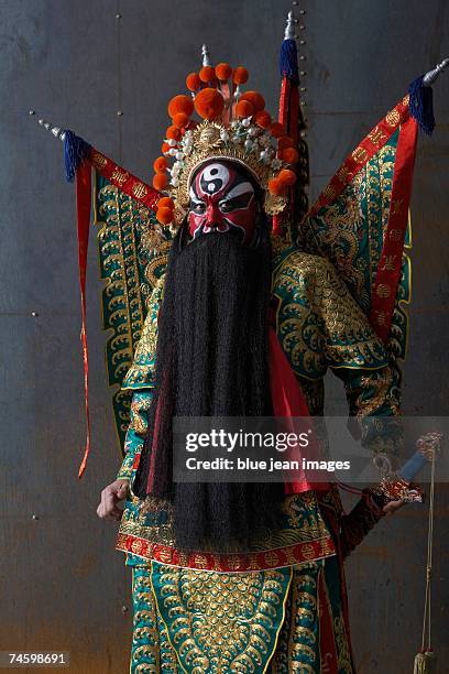 close up of an actor dressed as a traditional beijing opera army general posing fiercely in front of an industrial rusting steel wall with flags and a sword. - chinese opera makeup stock pictures, royalty-free photos & images