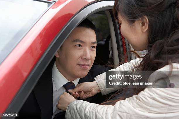 wife adjusts her husband's tie through the window of a car as he leaves for work - adjusting blue tie stock-fotos und bilder