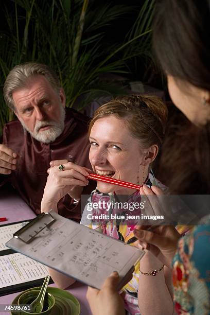woman gnaws on a pair of chopsticks as waitress presents the bill - waitress booth stock pictures, royalty-free photos & images