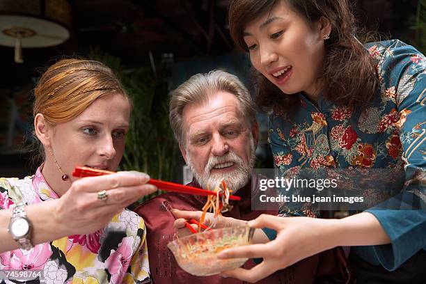 waitress holds up a dish while man and woman use chopsticks to take food from it - waitress booth stock pictures, royalty-free photos & images