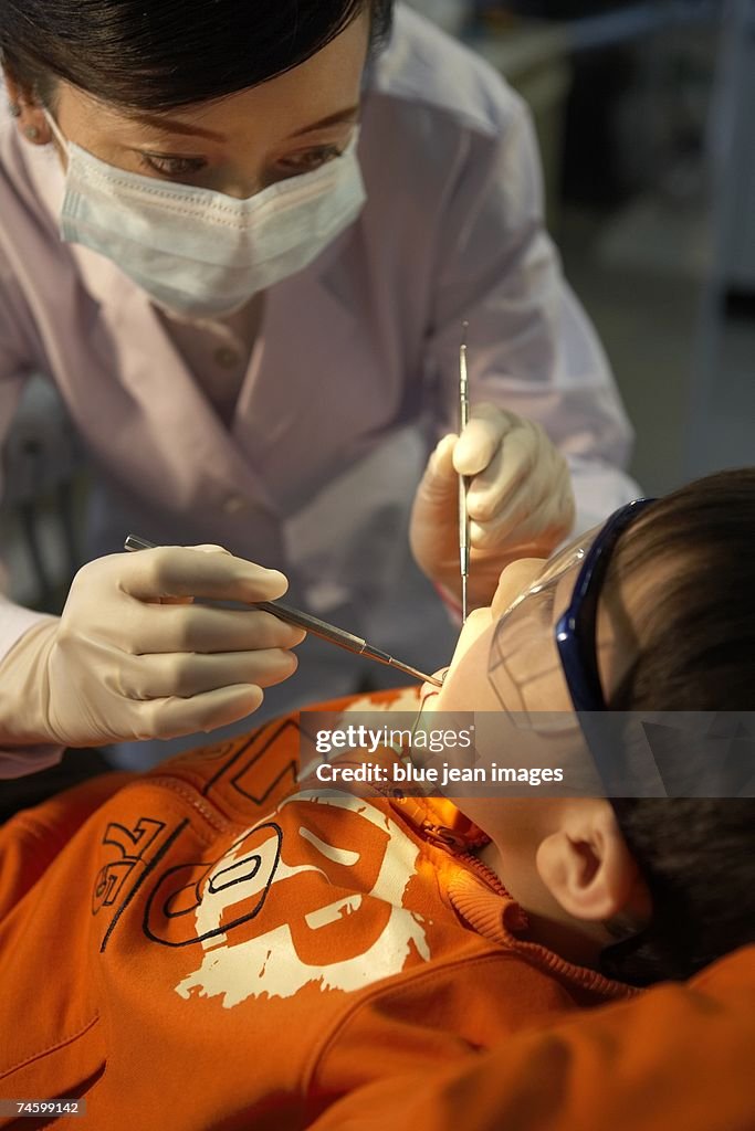 A female dentist examines a fearful child patient with her dental instruments (over shoulder view).