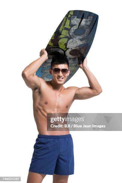 young muscular man with surfboard - zwembroek stockfoto's en -beelden