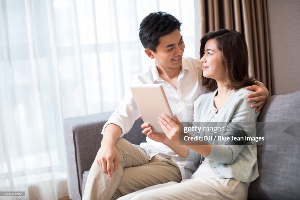 Cheerful young couple using digital tablet at home