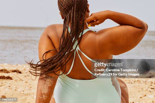 young woman sitting on the beach - badebekleidung stock-fotos und bilder