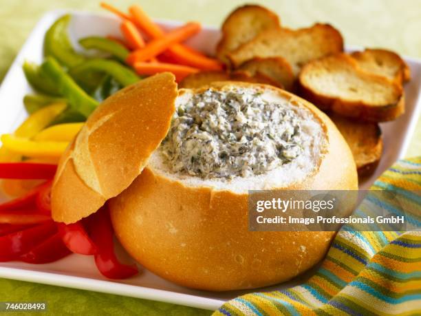 spinach dip in a bread bowl with sliced veggies and toasted bread slices for dipping - spinach dip stock pictures, royalty-free photos & images