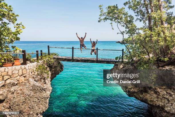 jamaica, negril, people jumping into ocean from footbridge - steilküste stock-fotos und bilder