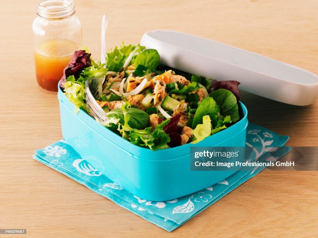 Mixed leaf salad with smoked salmon in a lunch box with a jar of dressing