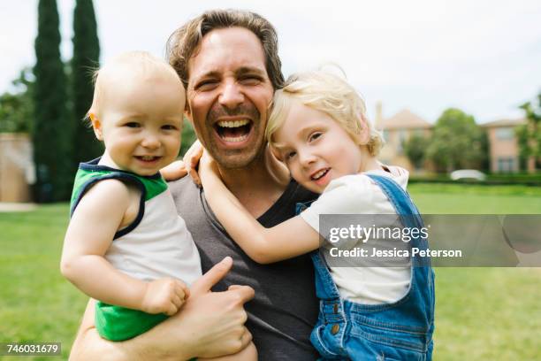 Portrait of father carrying sons (12-17 months, 4-5) in park