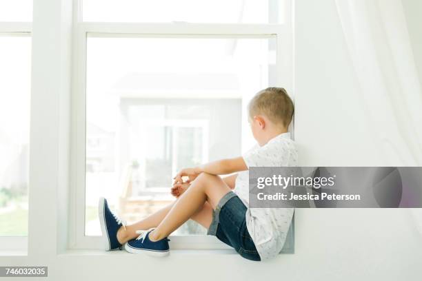 boy (7-8) looking through window - sitting on window sill stock pictures, royalty-free photos & images