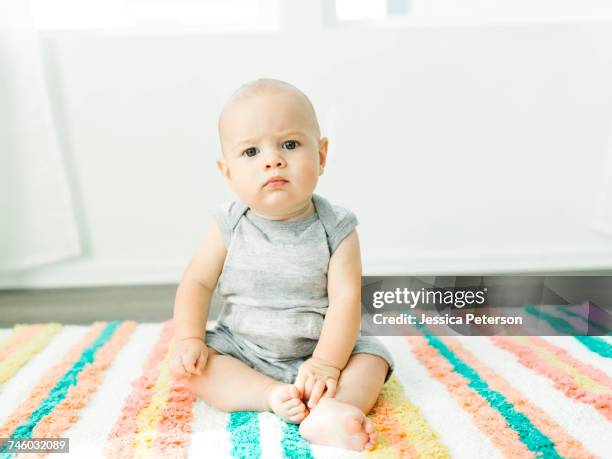 portrait of baby boy (6-11 months) sitting on colorful carpet - baby pout stock pictures, royalty-free photos & images