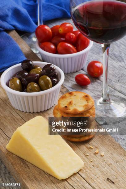 cheddar cheese, crackers, kalamata olives, tomatoes and a glass of red wine on a rustic wooden table - cheddar cheese stock pictures, royalty-free photos & images