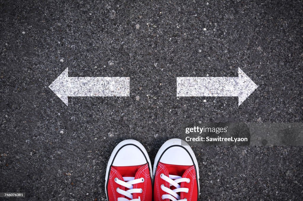 Directly Above Shot Of Person In Red Canvas Shoes By Arrow Signs In Opposite Direction On Road