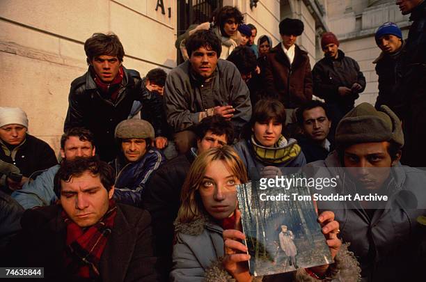 Group of people gathered for a protest in Bucharest, Romania, 1989. The young woman at the front is holding up a photograph.